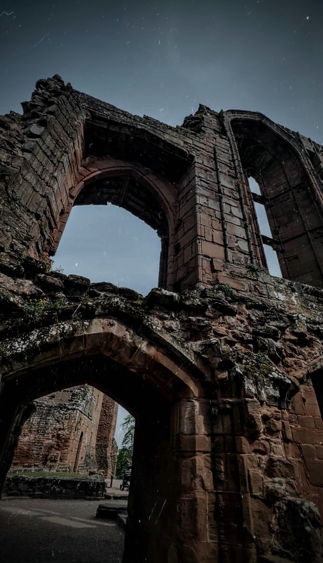 Ruined sandstone archways of a medieval barbican against a dusky sky