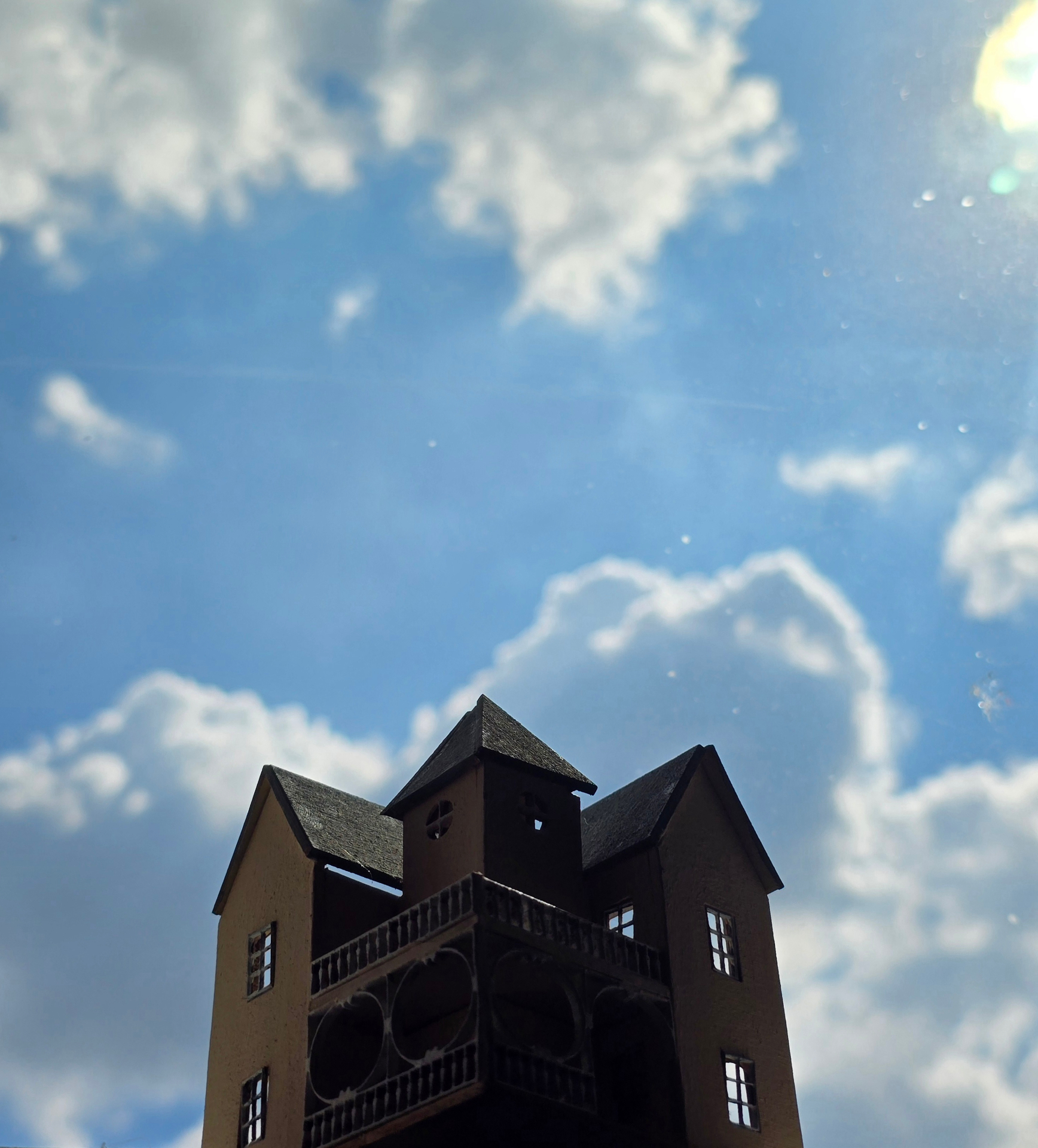 A miniature turreted house silhouetted against a vast blue sky filled with billowing clouds