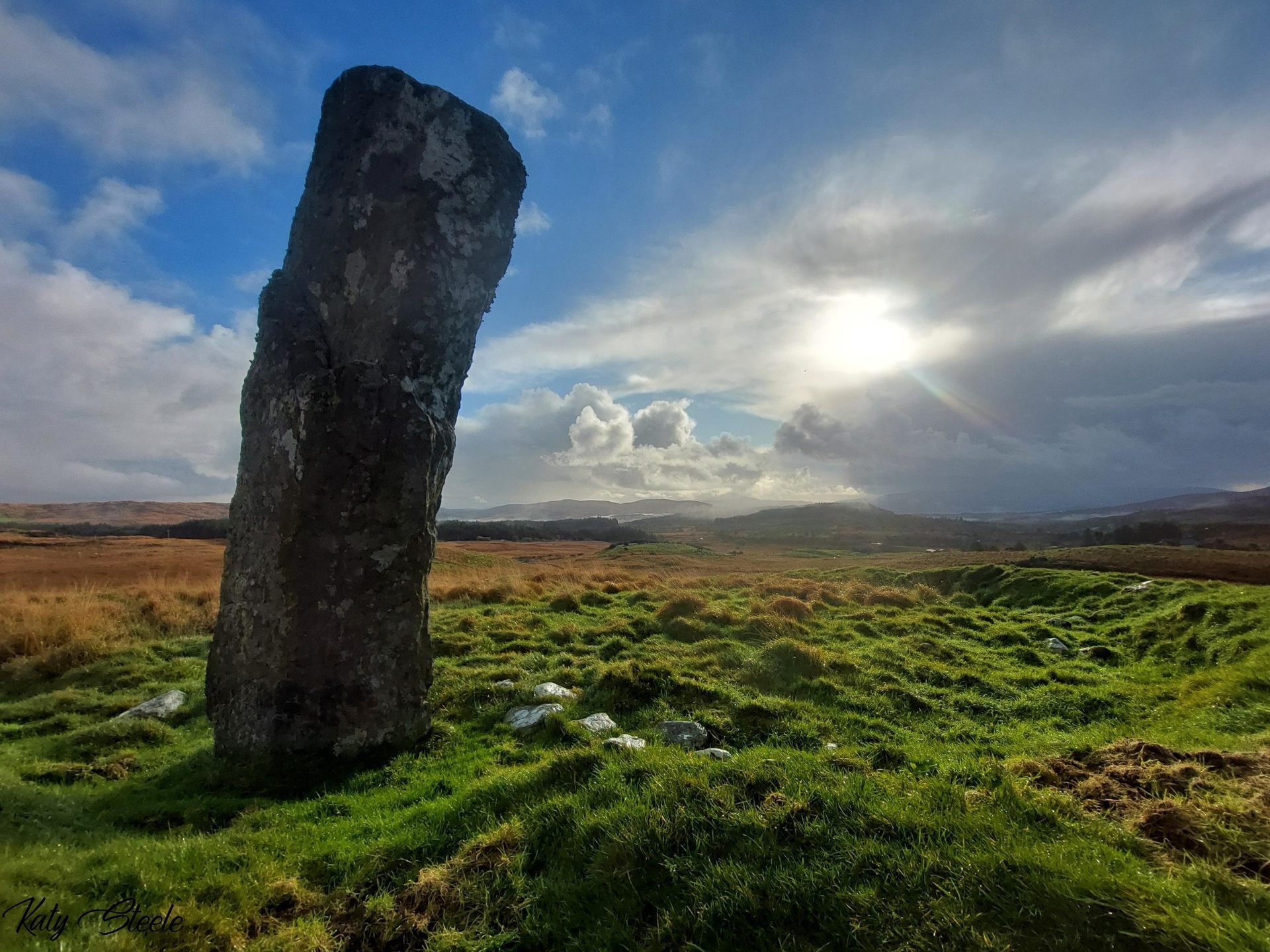 A weathered standing stone on a green Irish moor under a bright sunlit sky