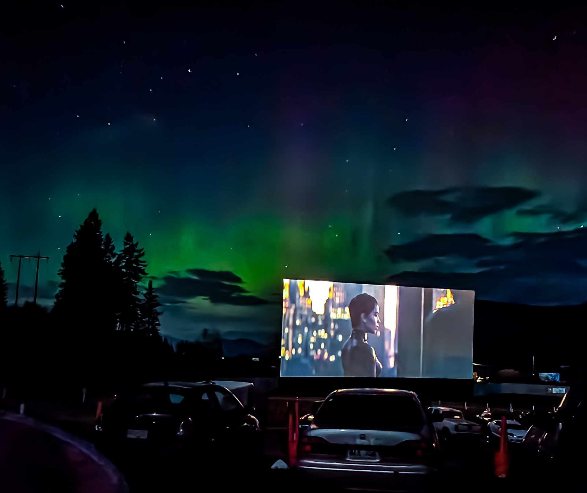 A drive-in movie screen glowing beneath an aurora-lit starry sky