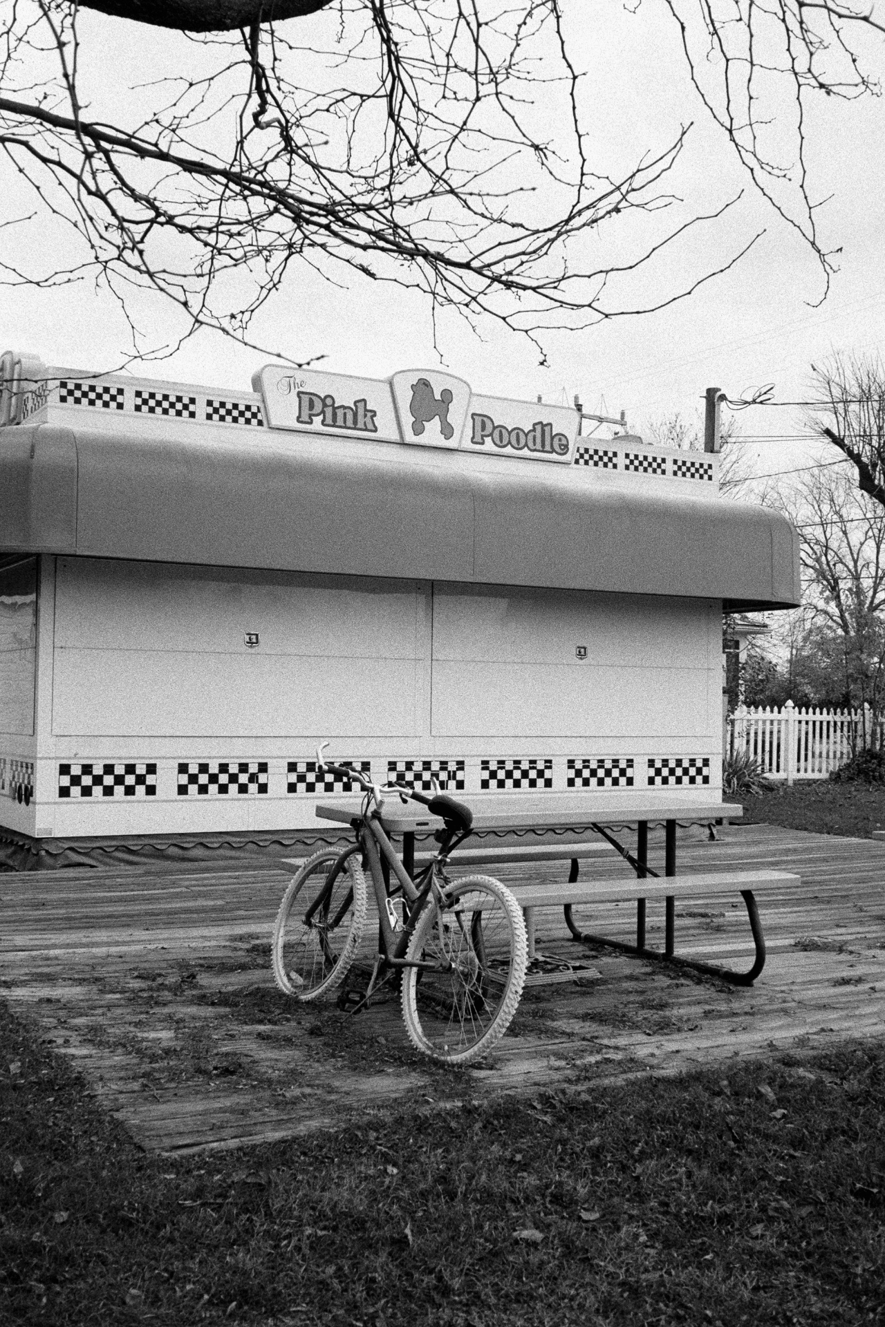 A bicycle leaning on a picnic table outside The Pink Poodle diner in black and white