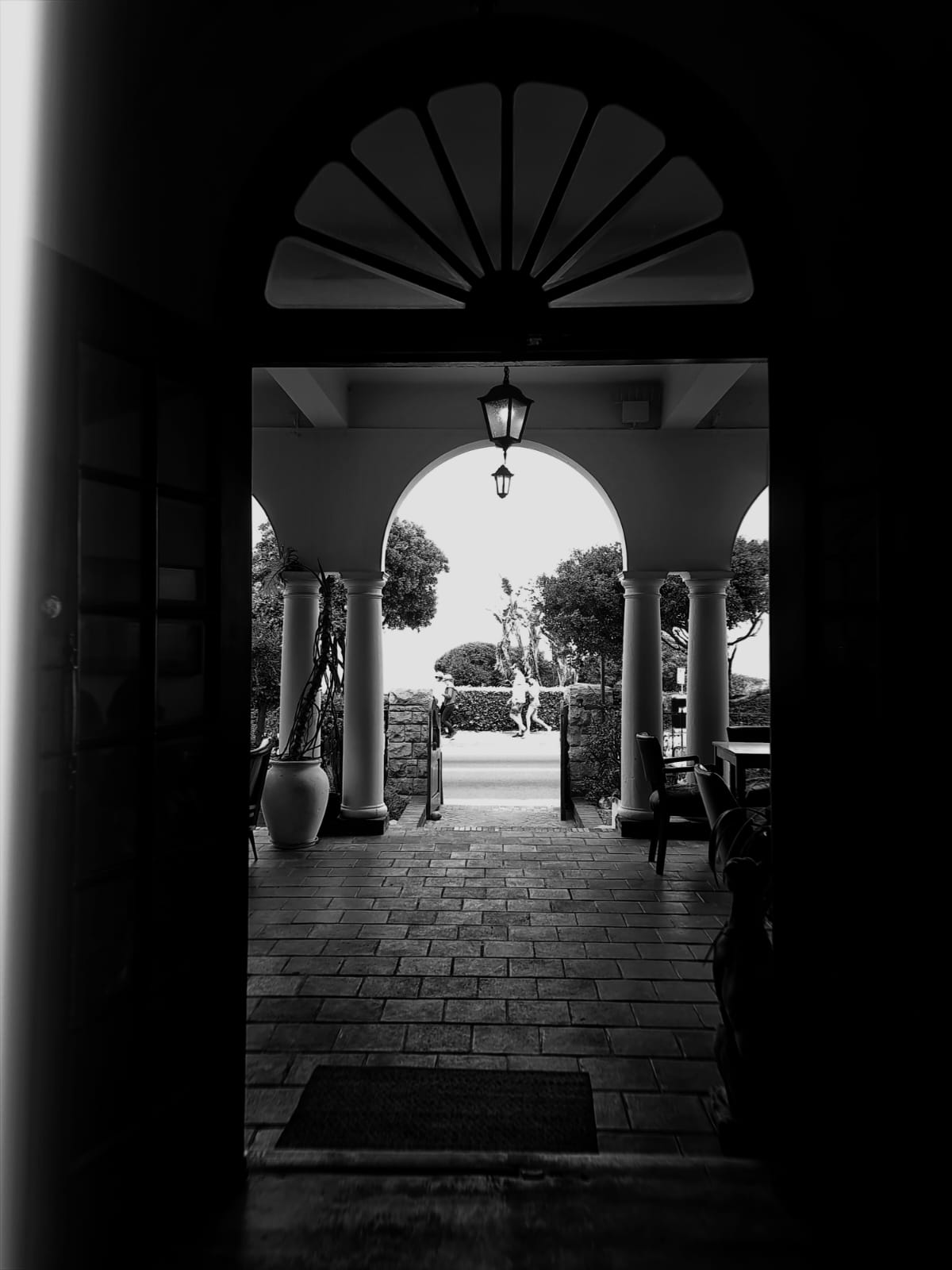 Black and white view through a doorway out to an arched colonnade and sunlit garden beyond