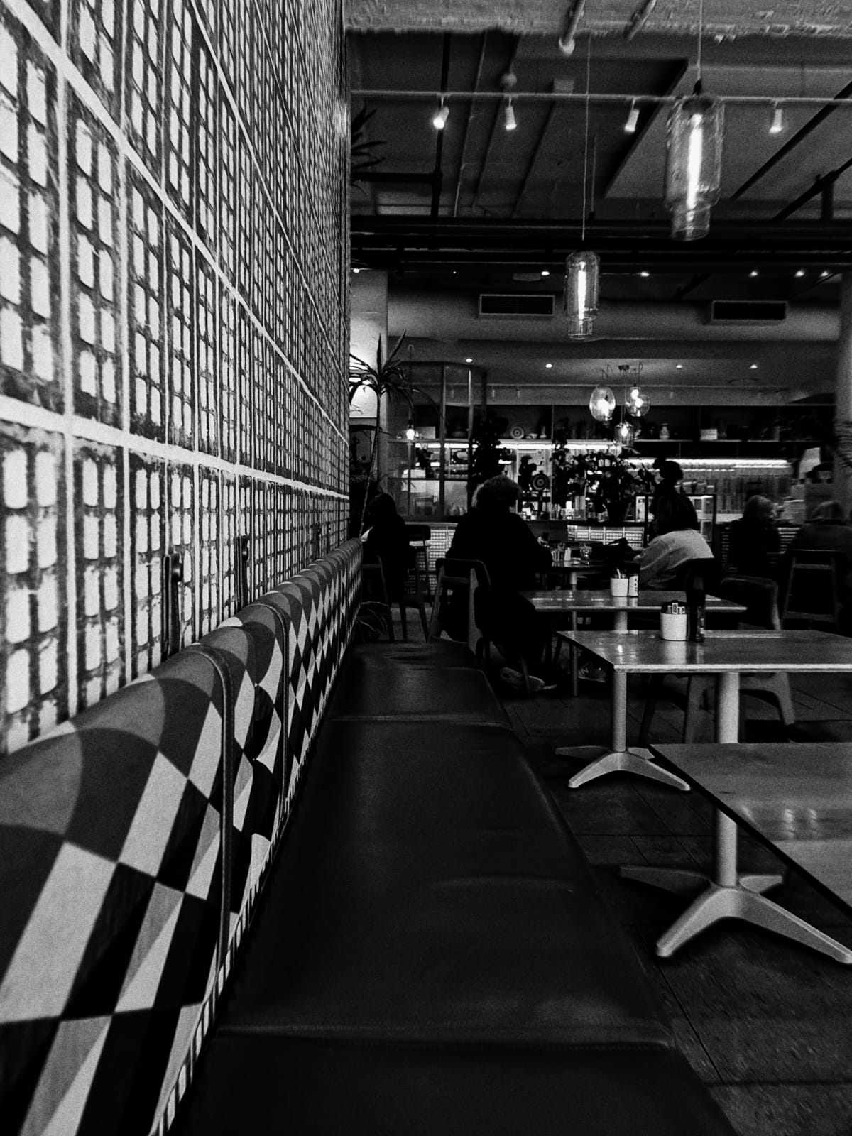 Black and white interior of a modern cafe with a long banquette, checkered upholstery, and pendant lights
